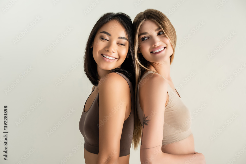 blonde woman and happy asian model while posing isolated on white - obrazy, fototapety, plakaty 