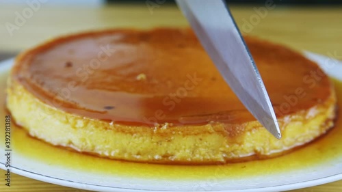 closeup man hands by knife cut soft milk flan with caramel syrup on white plate