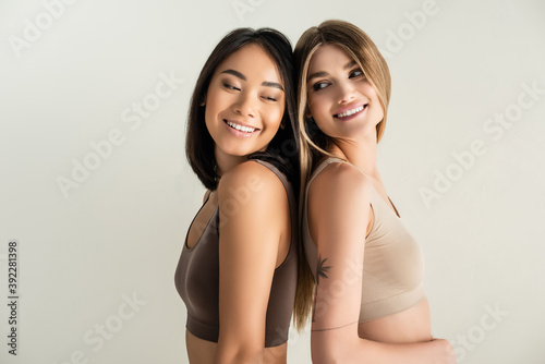 blonde woman and happy asian model while posing isolated on white