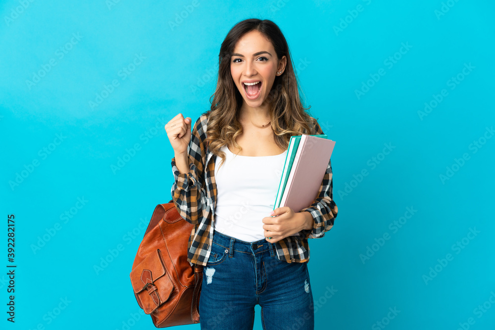 Young student woman isolated on blue background celebrating a victory in winner position - obrazy, fototapety, plakaty 