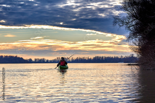 Woman kayaking on green kayak in winter Danube river at sunset. Back view. Concept: adventure, holiday, vacation © watcherfox