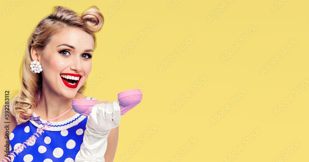 Call center. Happy woman with phone, in blue pin-up style dress in polka dot, with copy space for slogan or text, isolated over yellow background. Pinup girl in retro, vintage studio concept. Call center. Happy woman with phone, in blue pin-up style dress in polka dot, with copy space for slogan or text, isolated over yellow background. Pinup girl in retro, vintage studio concept.