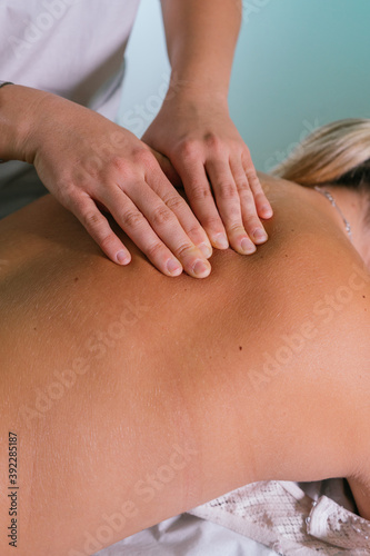 From above crop hands of professional therapist doing massage of female back in wellness salon