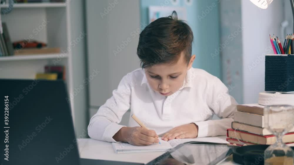 Focused little kid taking notes during an online class Focused little kid taking notes during an online class