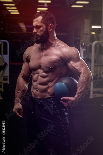 strong young bearded caucasian male with heavy training ball in dark gym
