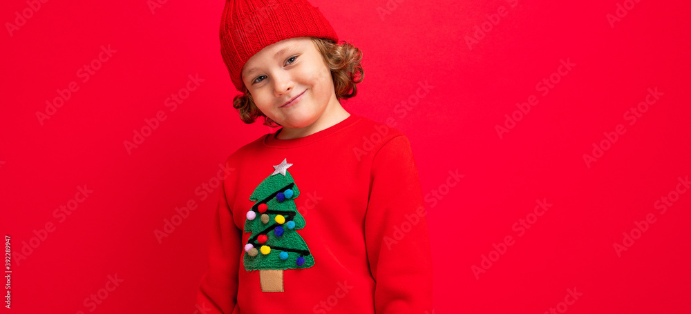 cool boy with curls on a red background in a sweater with a christmas tree cool boy with curls on a red background in a sweater with a christmas tree