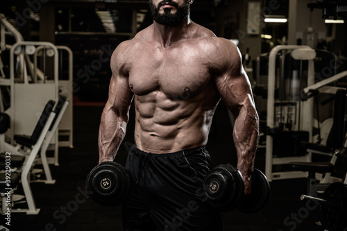 strong athlete bearded man with perfect body muscle with iron dumbbells in fitness sport night gym