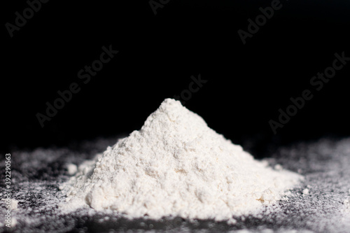 A mound of white flour on a dark surface. Side view.