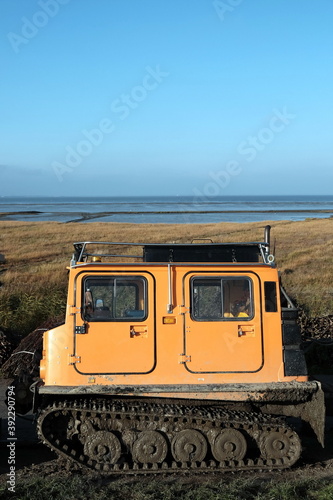 Kettenfahrzeug in leuchtendem Orange für den Lahnungsbau im Watt am Deich bei Bensersiel und Esens im Herbst an der Küste der Nordsee in Ostfriesland in Niedersachsen photo