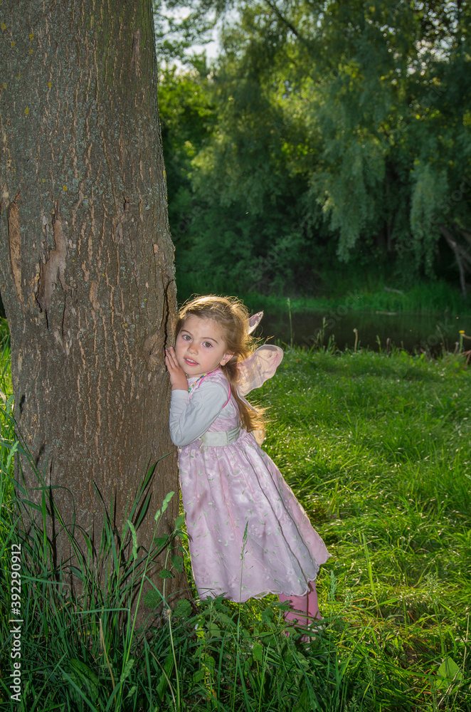 A little girl with butterfly wings among the green grass in the backlight with sun glare. Selective focus. A little girl with butterfly wings among the green grass in the backlight with sun glare. Selective focus.