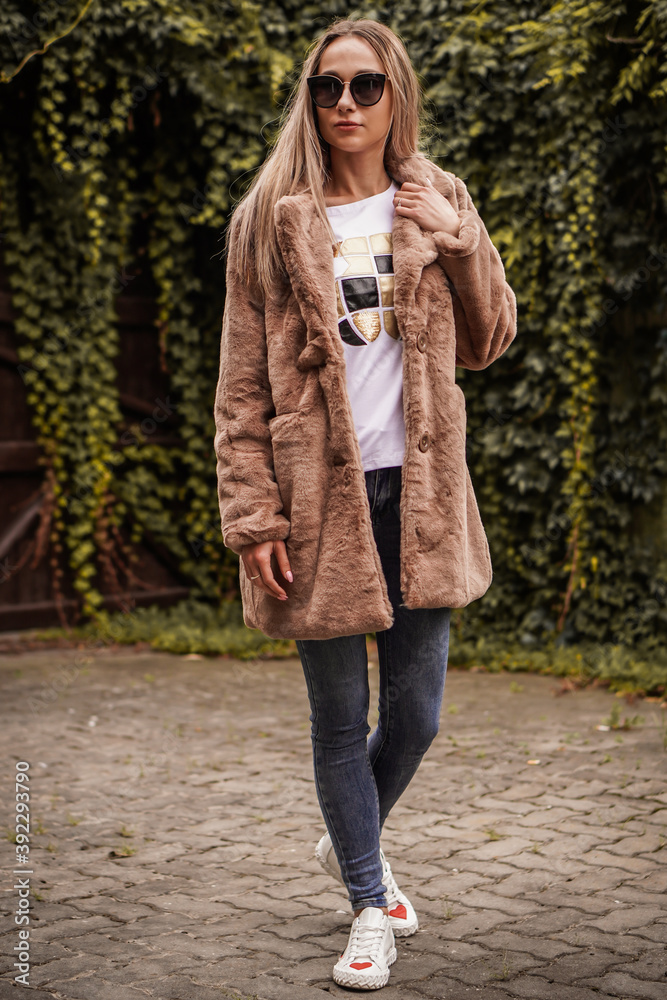Young blond-haired fashion model takes photos for a fashion store outdoors with a blurred background. Young blond-haired fashion model takes photos for a fashion store outdoors with a blurred background.