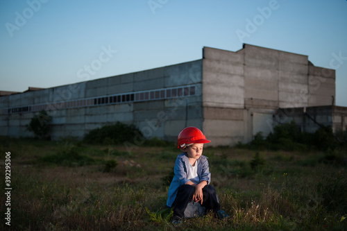 dismissal and unemployment concept of upset sad little boy red helmet sitting on tool box on idustry factory plant background photo