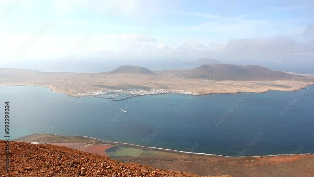 Magnificent views of La Graciosa island with ferry boat heading from pier to Lanzarote on sunny day. Natural volcanic landscape from Mirador del Rio viewpoint Magnificent views of La Graciosa island with ferry boat heading from pier to Lanzarote on sunny day. Natural volcanic landscape from Mirador del Rio viewpoint