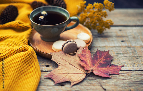 Autumn, fall leaves, hot steaming cup of tea and a warm scarf on rustic wooden table background. Seasonal, morning tea, sunday relaxing on the garden and still life.