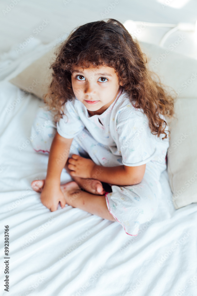 Naklejka premium Beautiful little curly girl in the bedroom on the bed