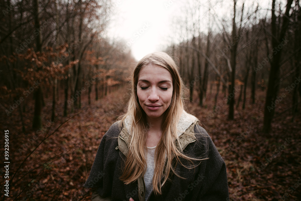 Long haired woman in warm clothes standing among trees with peacefully closed eyes Long haired woman in warm clothes standing among trees with peacefully closed eyes
