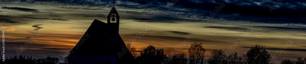 Panorama, Umrisse einer Kirche und Silhouetten von Bäumen vor einem Sonnenuntergang Himmel