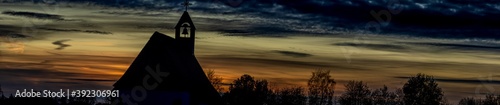 Panorama, Umrisse einer Kirche und Silhouetten von Bäumen vor einem Sonnenuntergang Himmel