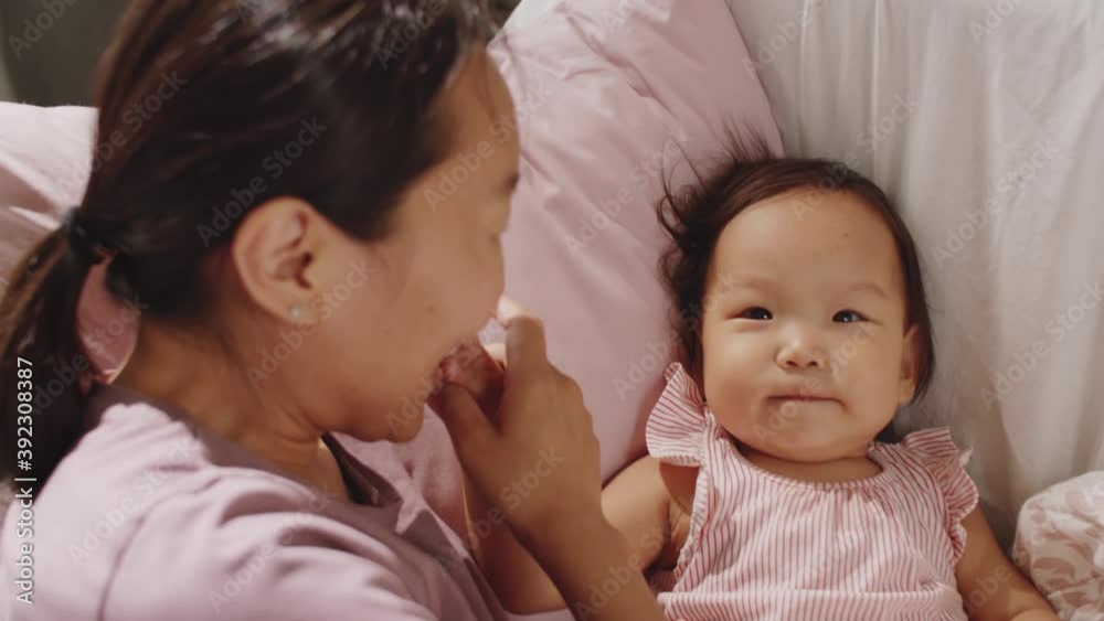 High angle close up shot of joyous Asian woman lying on sofa with happy toddler daughter, kissing and bonding with her High angle close up shot of joyous Asian woman lying on sofa with happy toddler daughter, kissing and bonding with her