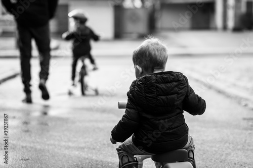 Two young boys ride bikes in a suburban driveway. photo