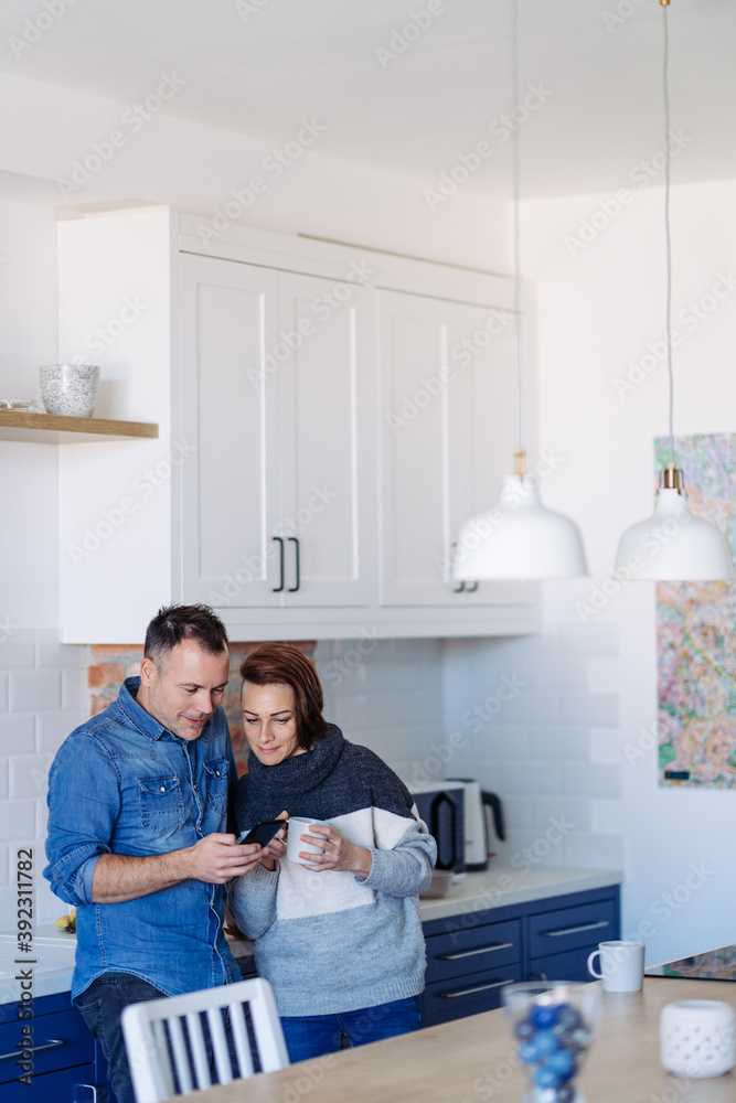 Couple standing in the kitchen drinking coffee and using smartphone Couple standing in the kitchen drinking coffee and using smartphone