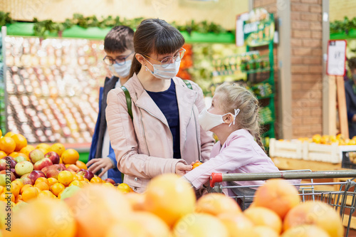 Foto Mom with children in protective masks in a grocery store choosing fruits