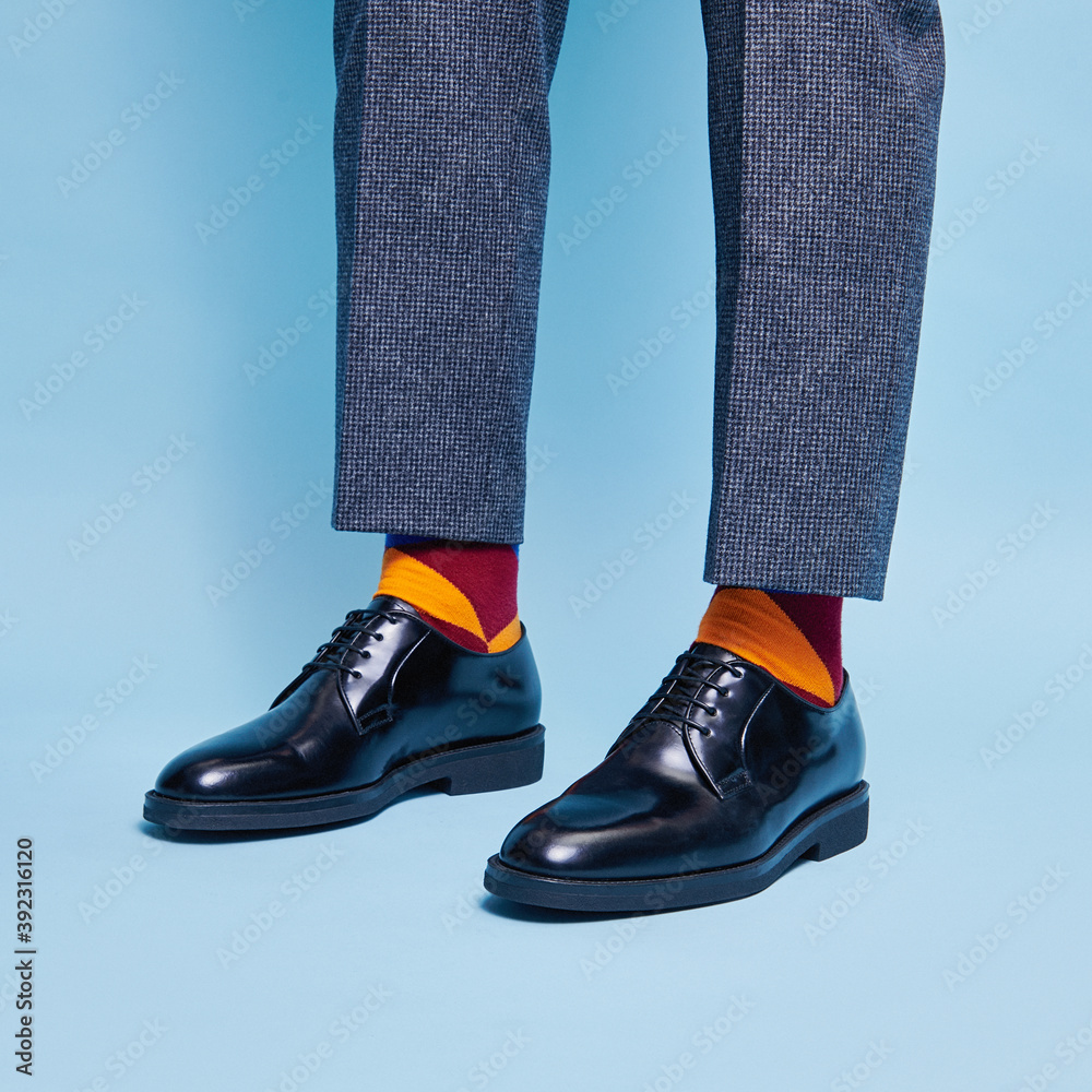 A man in handmade Italian leather shoes and colored funny socks stands on a blue background A man in handmade Italian leather shoes and colored funny socks stands on a blue background