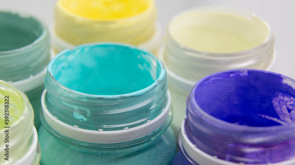 Jars of acrylic paint in green, blue, yellow shades close-up.