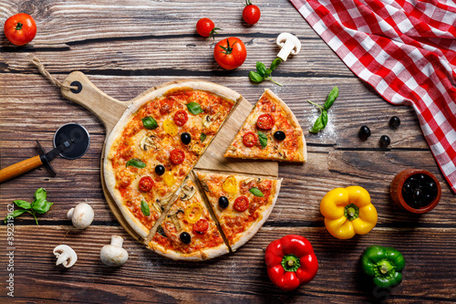 Deliciosa pizza italiana en la mesa de madera para la vista superior del restaurante italiano con verduras como pimientos, champiñones, mozzarella, tomate, jamón, aceitunas, aceite y orégano photo