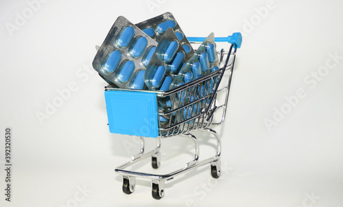 blue grocery cart with blisters of blue color capsules on white background, pharmaceutical business concept, pandemic photo