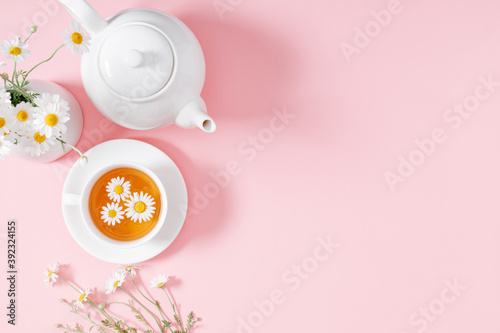 White chamomiles, cup and teapot on pastel pink background. Herbal tea of chamomile flower. Chamomile tea concept. Flat lay, top view, copy space
