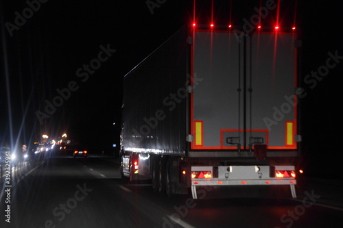 Obraz na płótnie Semi trailer truck with lighting reflection stripe on rear board move on dry asphalted night road in dark, back view - intrenational transportation logistics w salonie