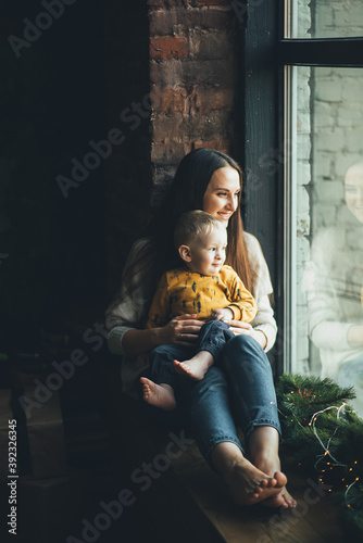 Young beautiful mother with her cute boy. Portrait of mom and little son near a chic Christmas tree