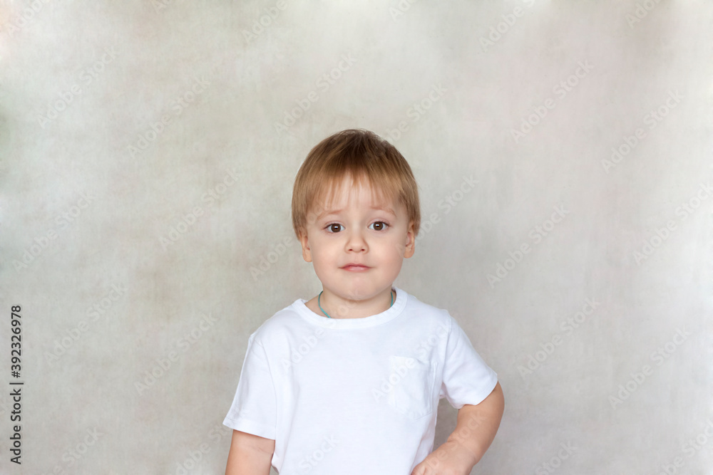 Naklejka premium Portrait of a cute little boy in a white t-shirt. Children's emotions. Child on the background of the wall. Success, bright idea, creative ideas and concepts.