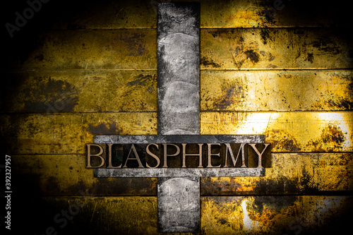 Blasphemy text message on upturned lead cross with textured grunge vintage gold background photo