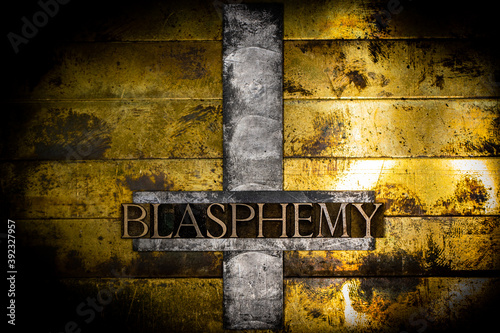 Blasphemy text message on upturned lead cross with textured grunge vintage gold background