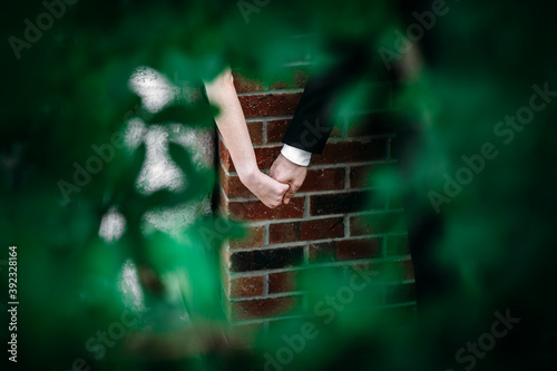 A man and woman holding hands around the corner without looking on their wedding day