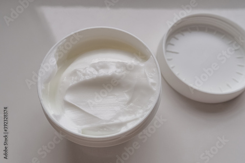 Opened white jar of cosmetic face cream with lid on a black slate background