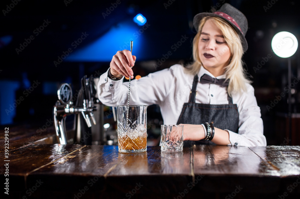 Expert woman barkeeper formulates a cocktail behind the bar