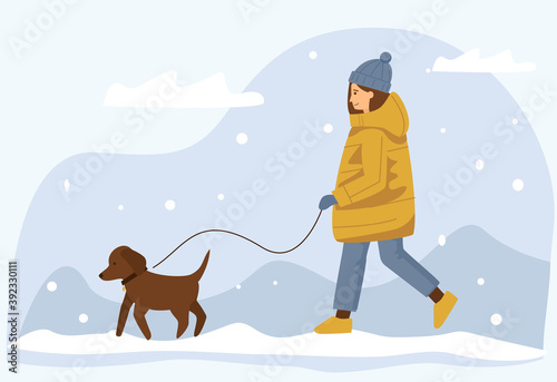 Woman in a warm jacket walks her dog in winter.