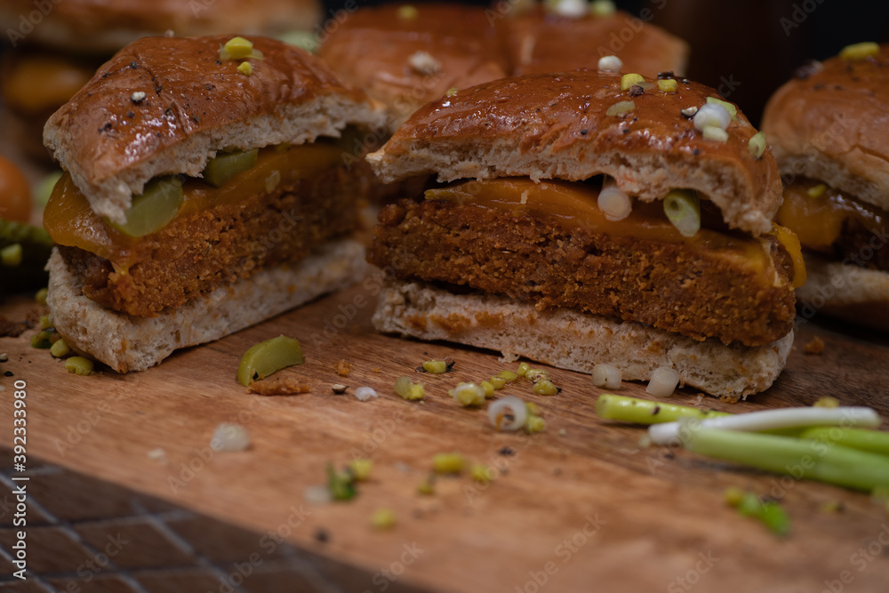 Vegan burgers made with seitan and vegan cheese, pickles on wooden cutting board Vegan burgers made with seitan and vegan cheese, pickles on wooden cutting board