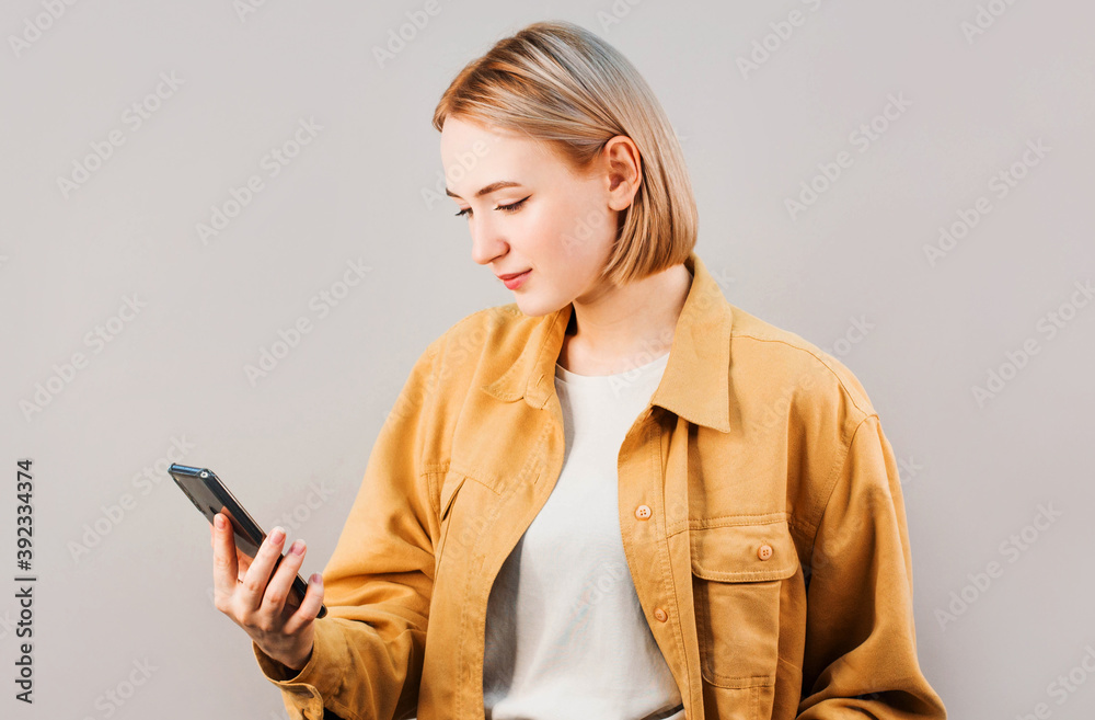 Smiling businesswoman using smartphone over gray background. Wearing in blue shirt and glasses. Smiling businesswoman using smartphone over gray background. Wearing in blue shirt and glasses.