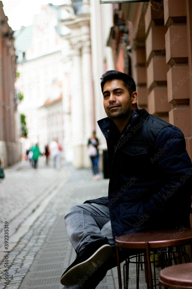 A south asian Indian ethnicity man sitting in an open street side restaurant located in central europe. Low angle shot of a smiling man looking at camera.
