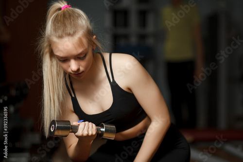 Girl fitness model posing with dumbbells in the gym. Athletic young woman posing and exercising fitness workout with weights. Shakes his biceps. Sport and health. Active lifestyle.