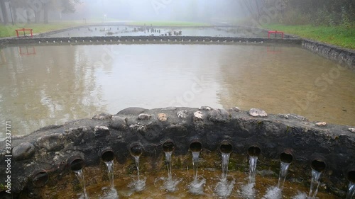 Misty morning haze over lazy river with water pipes in foreground. Autumn landscape in idyll nature. Scenic and atmospheric scenery near Sobec campground in Slovenia. Static shot, wide angle photo