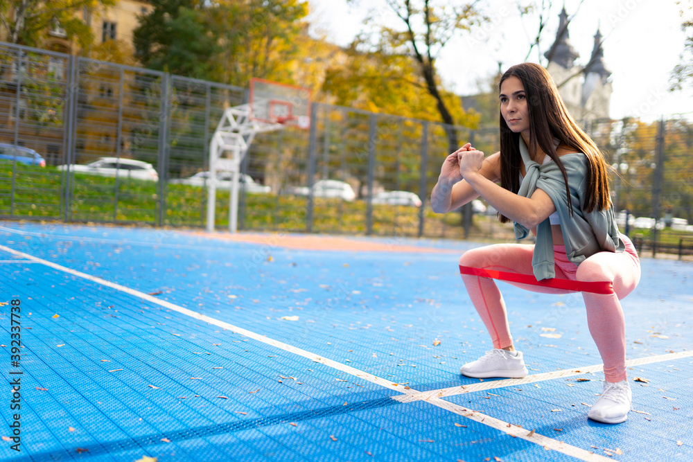 Obraz premium Athletic woman doing squats with resistance bands