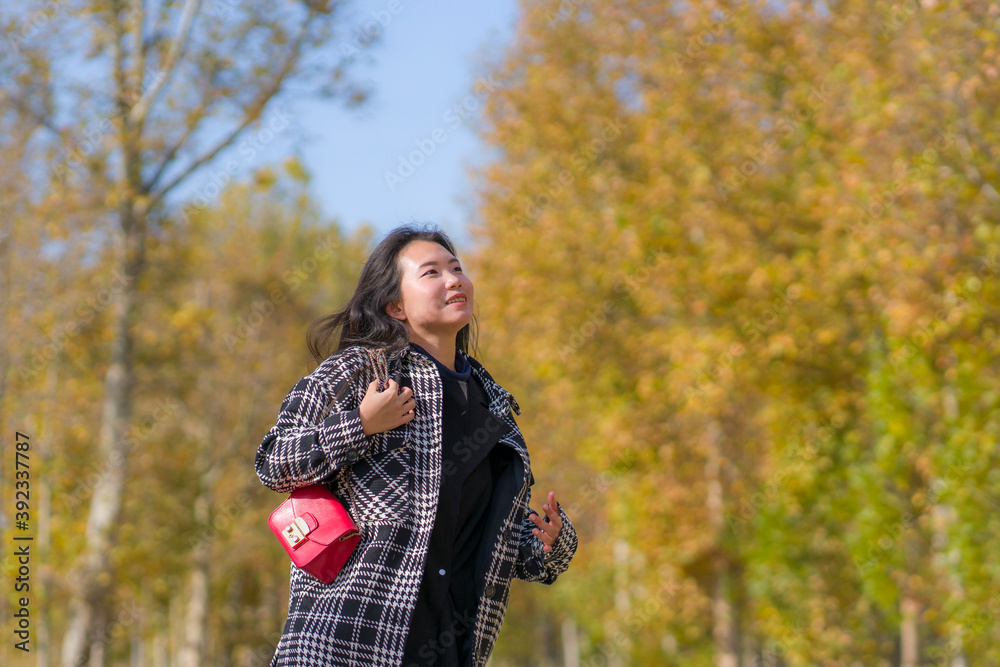 outdoors lifestyle portrait of young happy and pretty Asian Korean woman walking relaxed and cheerful at beautiful city park in vibrant yellow and orange Autumn tree leaves