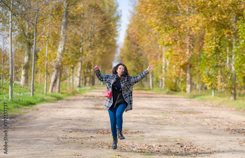 outdoors lifestyle portrait of young happy and pretty Asian Chinese woman jumping carefree and cheerful at beautiful city park in vibrant yellow and orange Autumn tree leaves