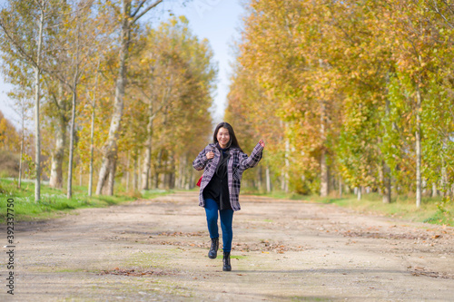 outdoors lifestyle portrait of young happy and pretty Asian Chinese woman jumping carefree and cheerful at beautiful city park in vibrant yellow and orange Autumn tree leaves © TheVisualsYouNeed