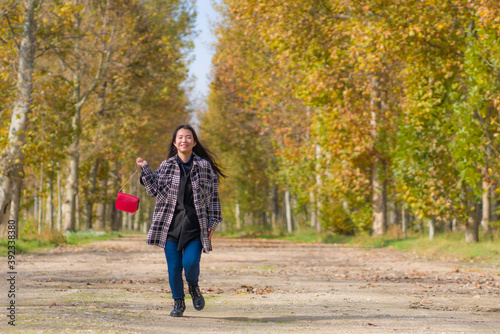 outdoors lifestyle portrait of young happy and pretty Asian Chinese woman walking relaxed and cheerful at beautiful city park in vibrant yellow and orange Autumn tree leaves © TheVisualsYouNeed